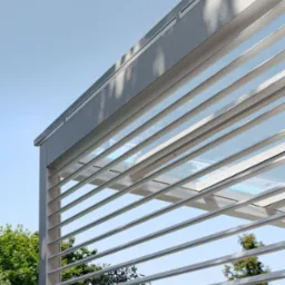 Nowoczesna pergola z regulowanymi lamelami w Łasku, zapewniająca cień i wentylację. Minimalistyczny design z widokiem na zieleń.