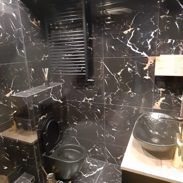 Elegancka łazienka z czarnymi płytkami imitującymi marmur, czarną armaturą i grzejnikiem drabinkowym.