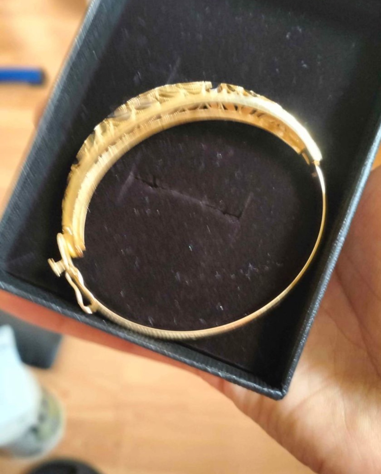 Złota bransoletka sztywna z ażurowym wzorem w czarnym pudełku prezentowym, widoczny mechanizm zapięcia.