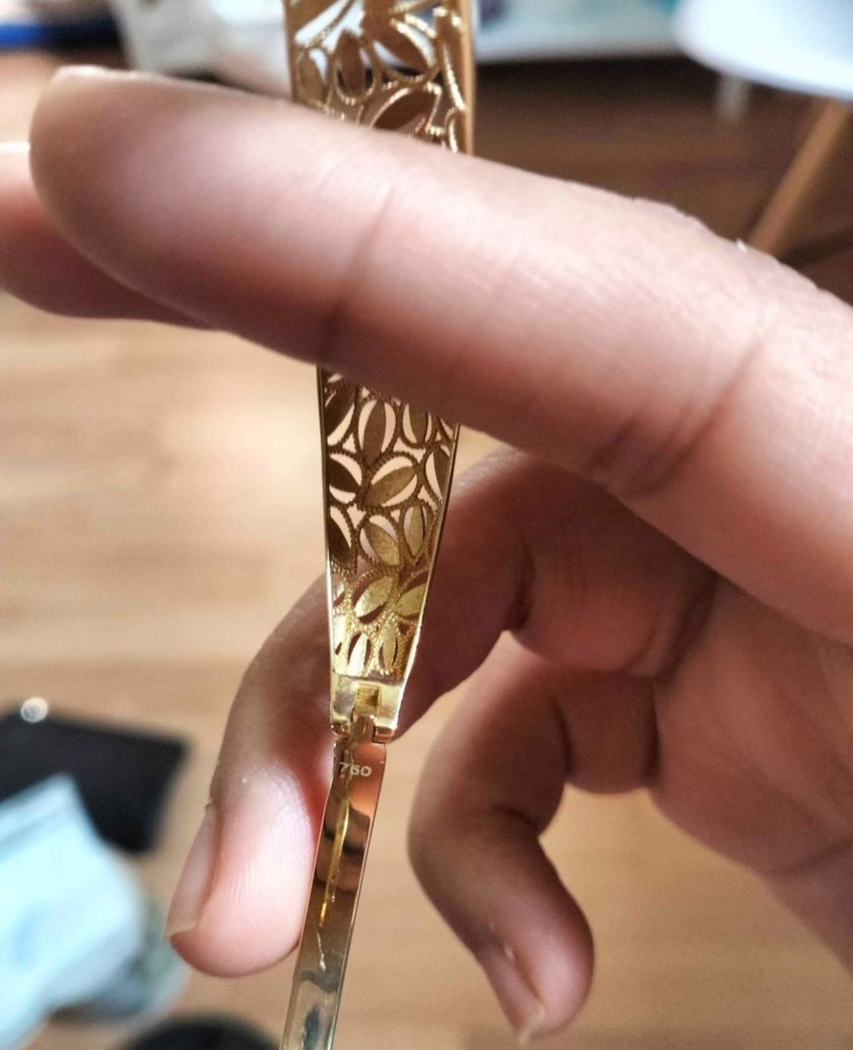 Delikatna złota oprawka okularów z wycinanym wzorem kwiatowym, trzymana w dłoni, widoczny numer 750.