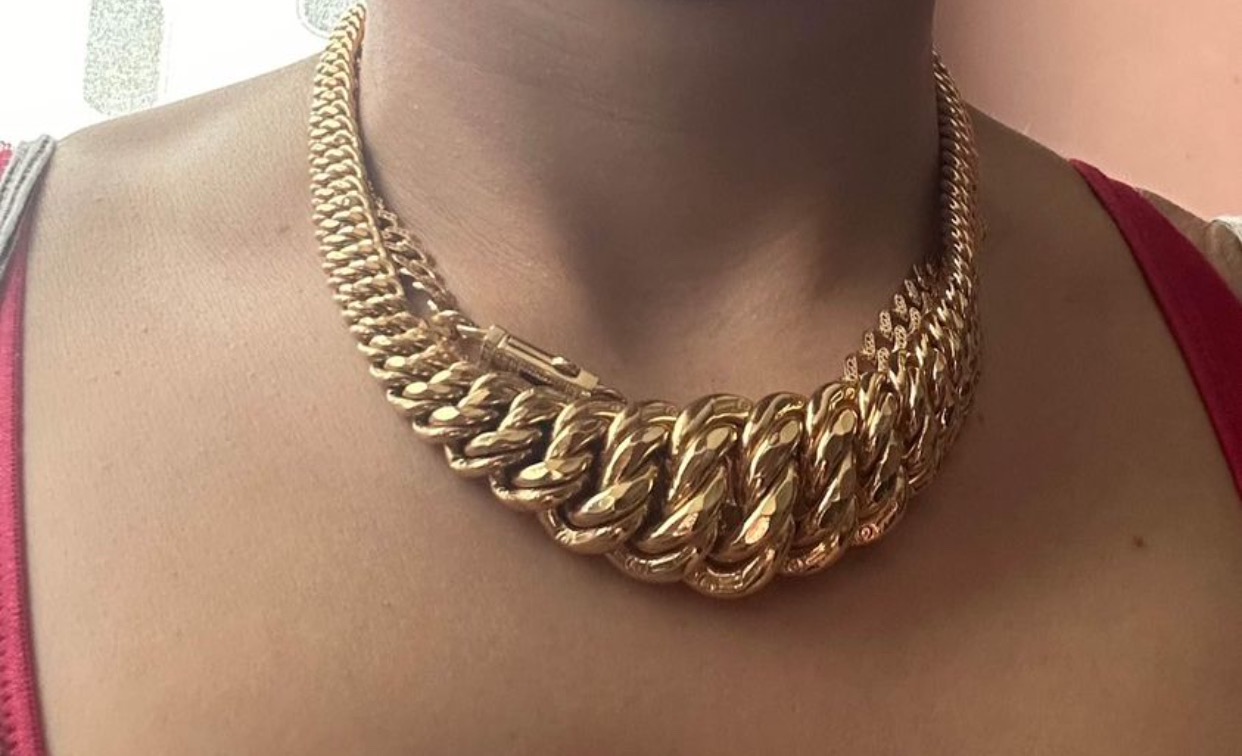 Masywny złoty łańcuch o splocie pancerka na szyi osoby, widoczny zamek z boku, czerwony ramiączko koszulki.