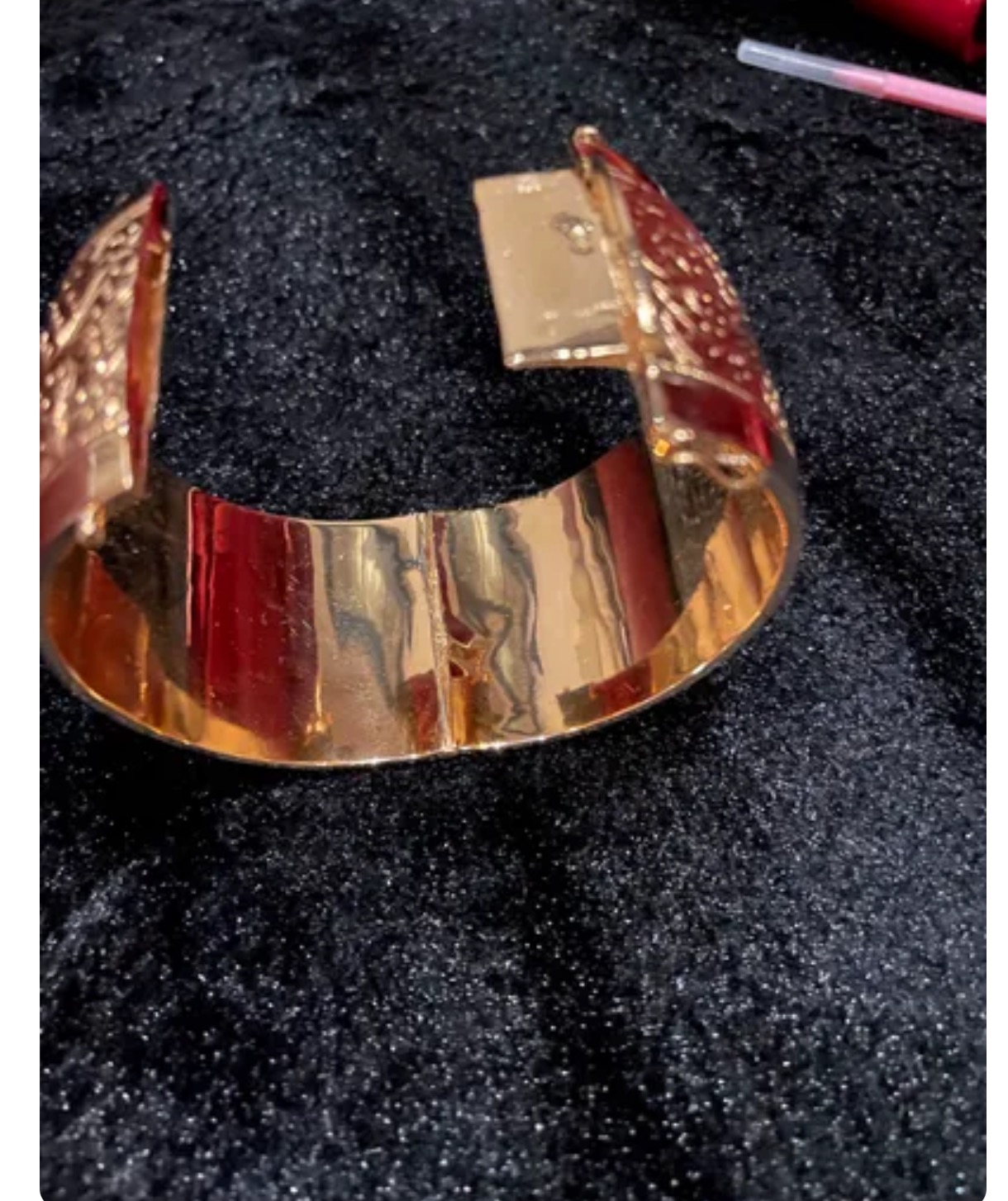 Złota, szeroka bransoleta z dekoracyjnym zapięciem na czarnym, teksturowanym tle, dostępna w Wąsoszu.