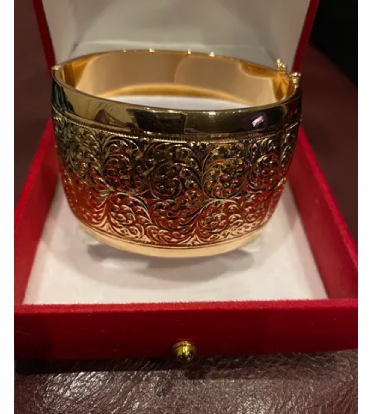 Złota, szeroka bransoleta z filigranowym wzorem w czerwonym pudełku prezentowym z aksamitnym wnętrzem.