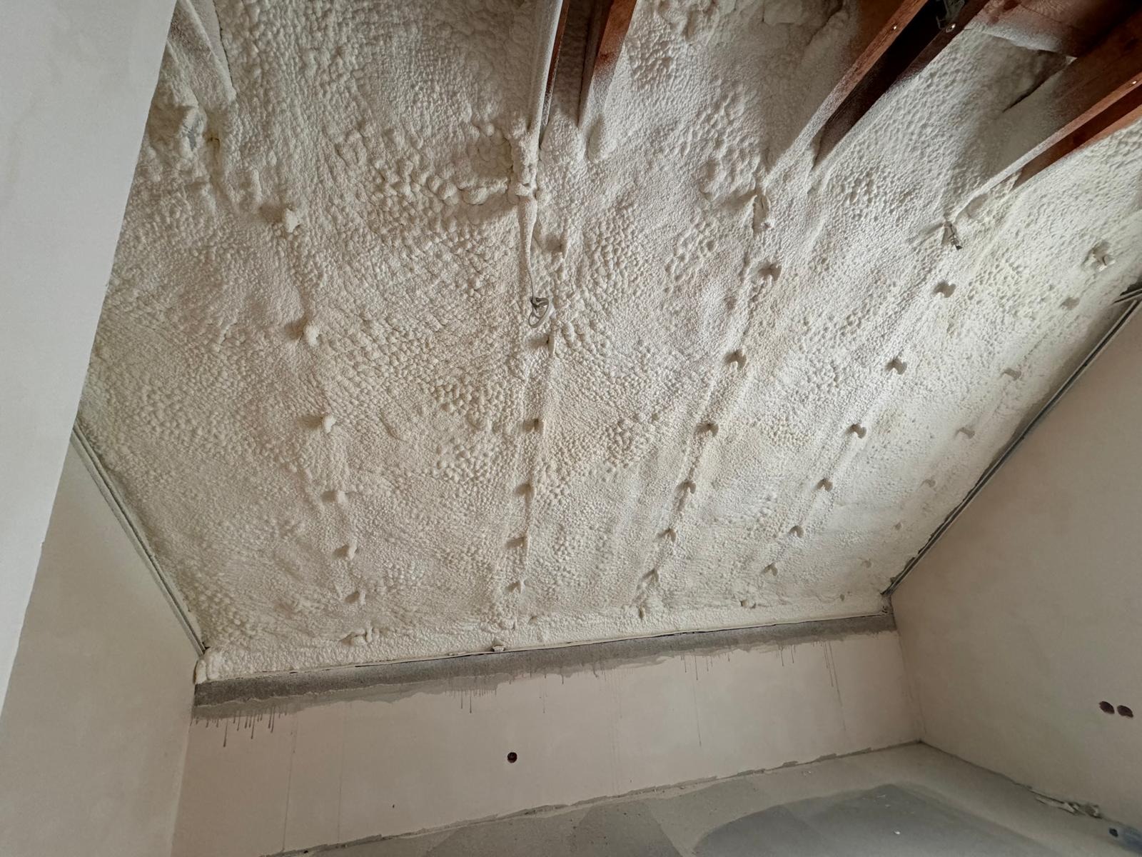 Poddasze z drewnianą konstrukcją pokryte warstwą pianki poliuretanowej, widoczne punkty mocowania, surowe ściany w tle.