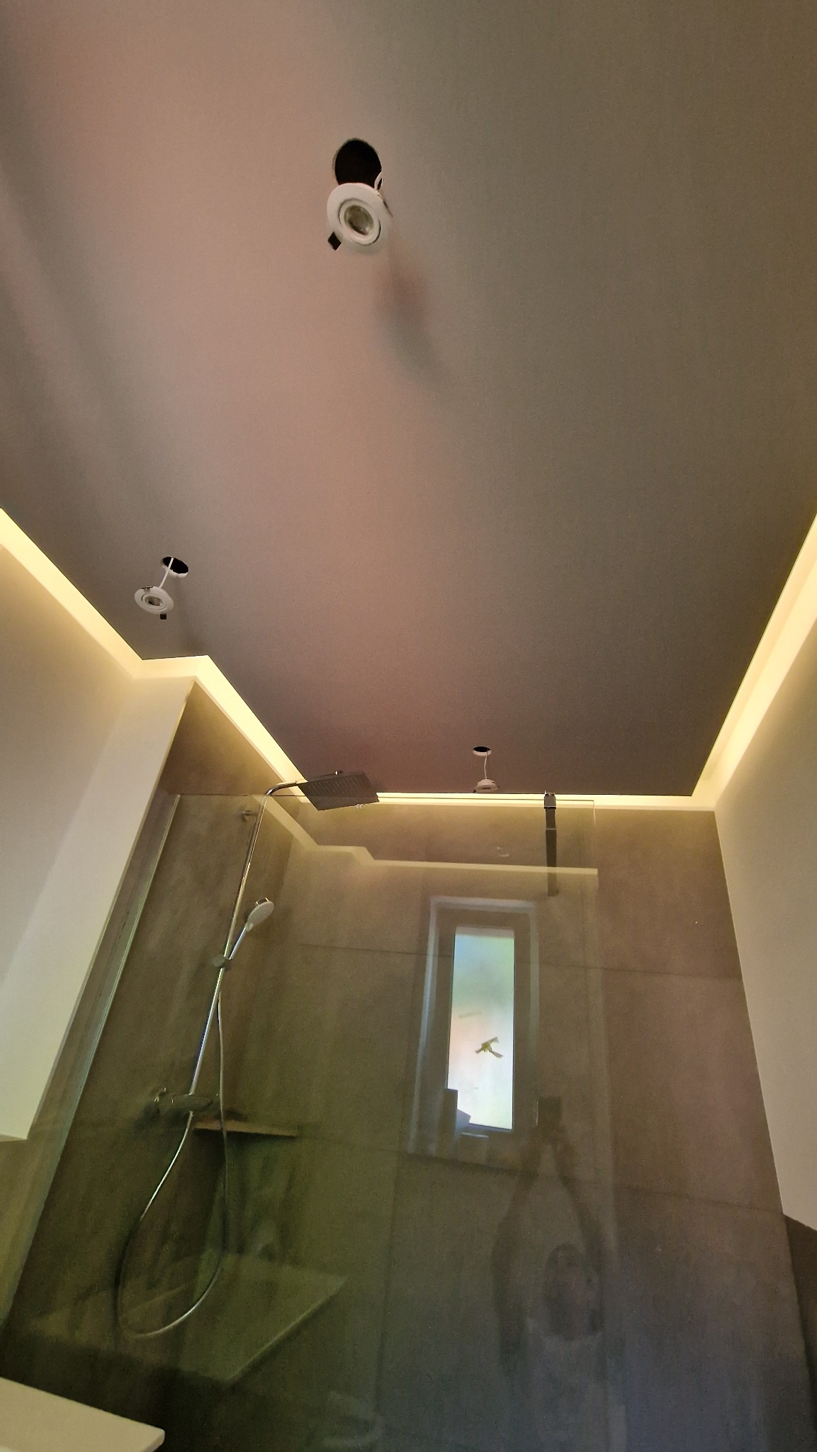 Nowoczesna łazienka z szarą ścianą prysznicową, oświetleniem LED w suficie i zamontowanymi punktowymi lampami sufitowymi, niektóre jeszcze bez żarówek.