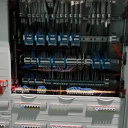 Rozdzielnica elektryczna z licznymi zabezpieczeniami, przewodami i listwami zaciskowymi, ukazująca kompleksową instalację.