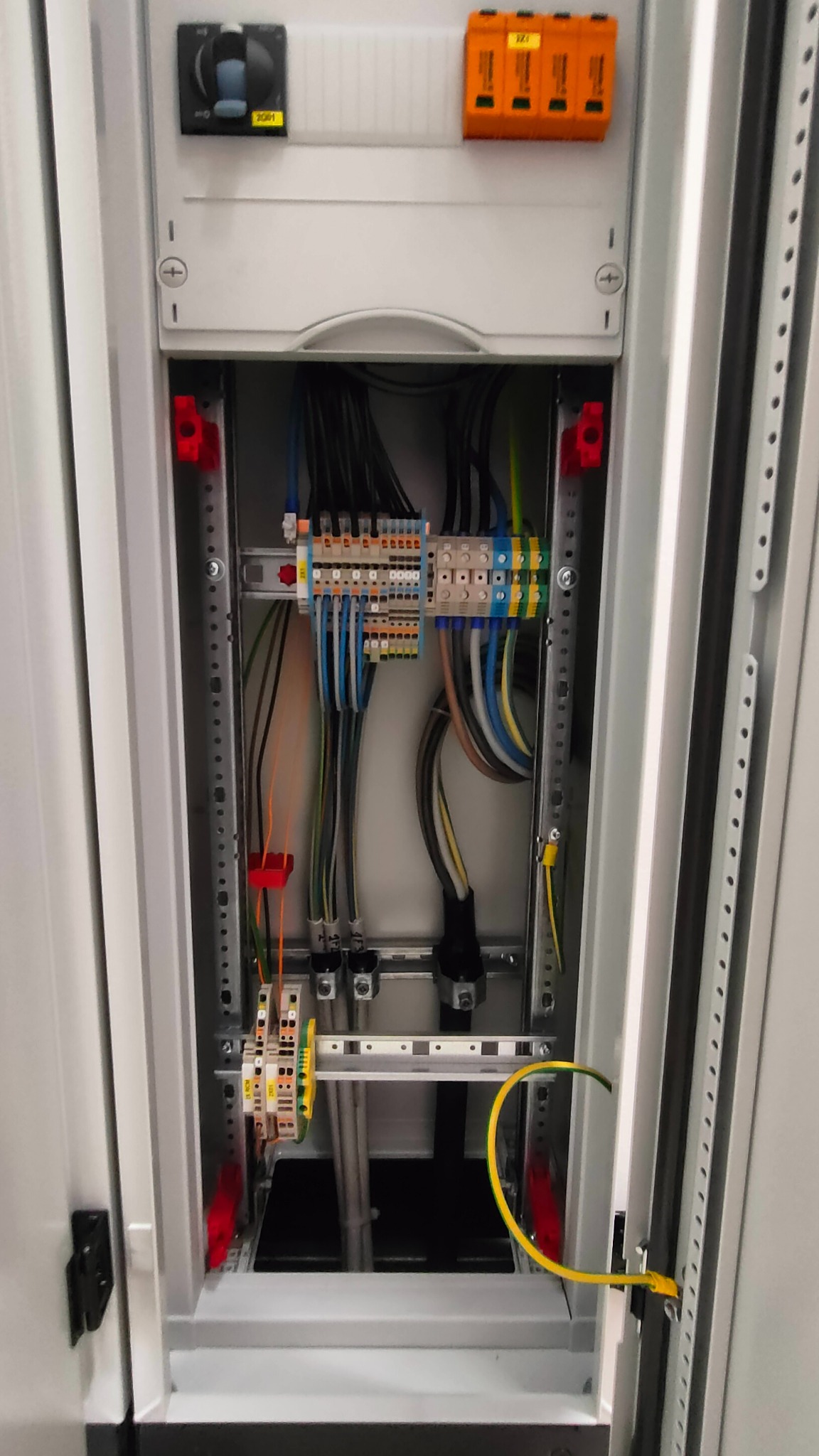 Wnętrze szafy rozdzielczej z widocznymi przewodami, listwami zaciskowymi i zabezpieczeniami, z żółto-zielonym przewodem uziemiającym, starannie ułożone kable w szynie montażowej.