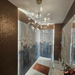 Atelier Projektowe GZDESIGN Gabriela Zięba - Nowoczesna łazienka z białymi marmurowymi płytkami, ścianą z motywem flamingów i designerskim, rozłożystym żyrandolem z kulistymi lampkami. Brązowe, teksturowane płytki na ścianie tworzą kontrast.