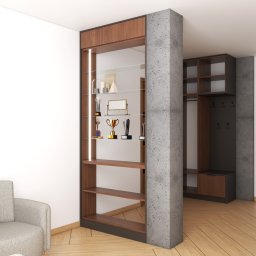 MEBLEZPACZKI.PL PROSTA SPÓŁKA AKCYJNA - Nowoczesna zabudowa przedpokoju z szafą wnękową i regałem ekspozycyjnym z trofeami, oddzielona betonowym filarem. Widoczny mężczyzna w garniturze.