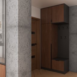 MEBLEZPACZKI.PL PROSTA SPÓŁKA AKCYJNA - Nowoczesna szafa wnękowa z drewna i szarości, z wieszakami i siedziskiem, wkomponowana w korytarz z betonową kolumną i drewnianą podłogą. Minimalistyczny design.