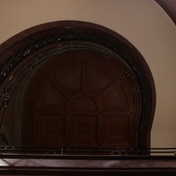 Jakub Bak - Wnętrze klatki schodowej z ciemnego drewna, z widoczną półokrągłą, zdobioną ścianą na końcu biegu schodów i metalową balustradą z okrągłymi elementami.