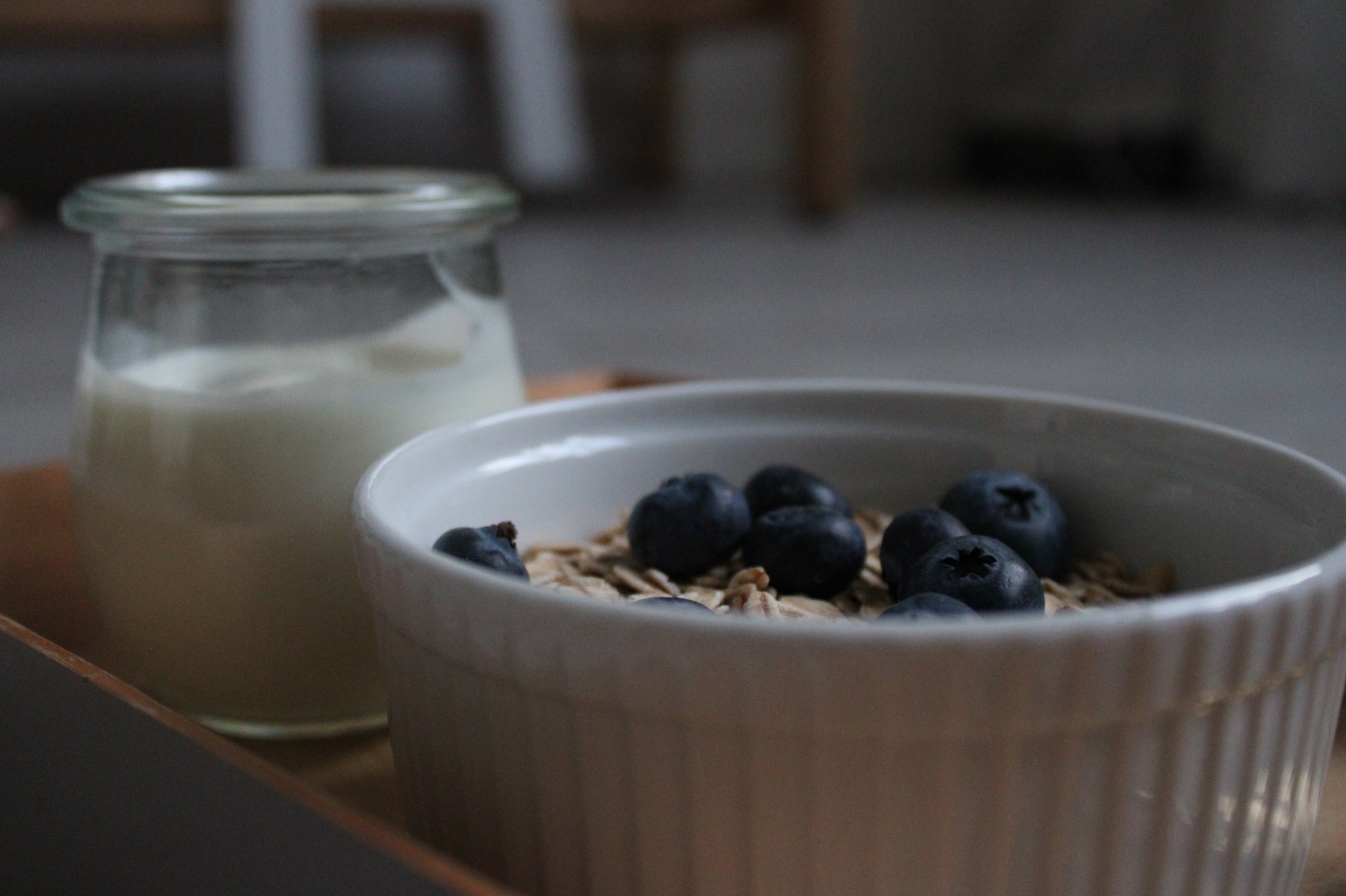 Śniadanie: jogurt w słoiku i miseczka z płatkami owsianymi i borówkami na drewnianej tacy.