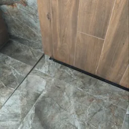 Szare marmurowe płytki podłogowe w łazience, połączone z pionowymi płytkami ściennymi imitującymi drewno, widoczny czarny profil dylatacyjny.