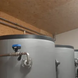 Rząd szarych, cylindrycznych zbiorników z rurami i czujnikami w pomieszczeniu z boazerią i białymi ścianami.