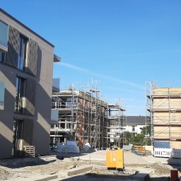 GONSKA DEVELOPMENT SPÓŁKA Z OGRANICZONĄ ODPOWIEDZIALNOŚCIĄ - Nowe budynki w trakcie wykańczania elewacji, widoczne rusztowania, przygotowane materiały budowlane i żółty agregat prądotwórczy.