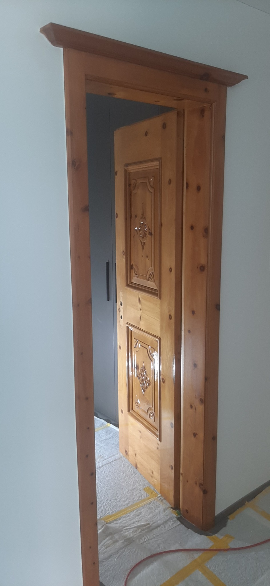 Odnowione drewniane drzwi wewnętrzne z dekoracyjnymi panelami, widoczne przez odrzwia, z zabezpieczoną folią podłogą.