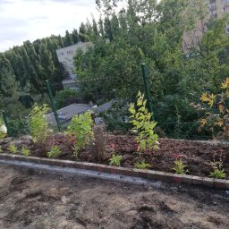 Marcin Kozłowski KozLOVEski - Nowo założony rabat kwiatowy z obrzeżem z cegieł i młodymi sadzonkami, widok na osiedle mieszkaniowe w tle.