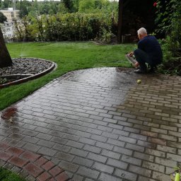 Marcin Kozłowski KozLOVEski - Mężczyzna w kucki przy mokrej kostce brukowej w ogrodzie, obok leży zielona piłka tenisowa, w tle trawnik z systemem nawadniania i budynek.