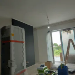 Wnętrze w trakcie prac wykończeniowych: pomalowana na ciemny kolor ściana, okno zabezpieczone folią, drabina oparta o ścianę, opakowania z materiałami budowlanymi i narzędzia malarskie na podłodze,...