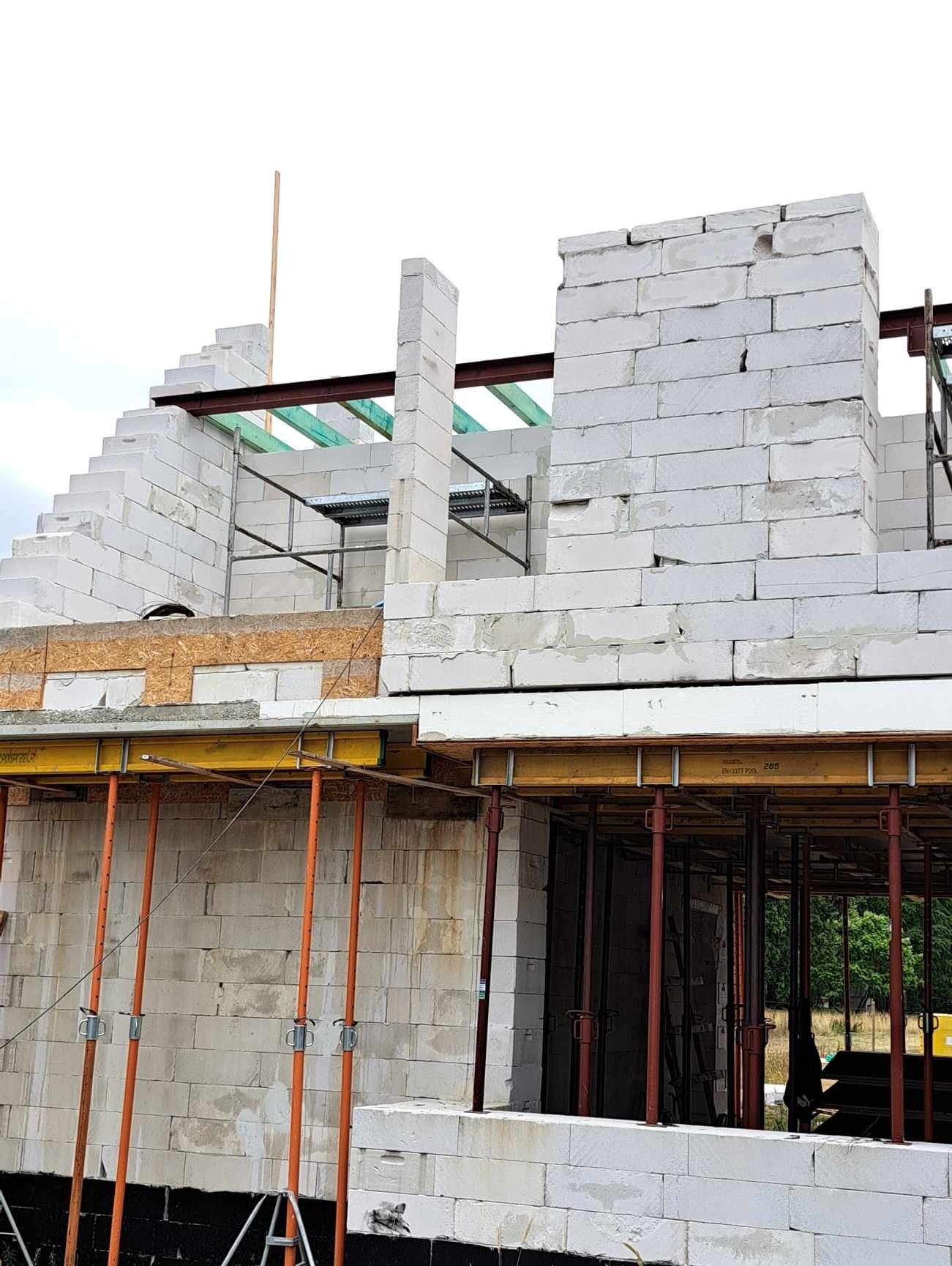 Budowa domu z białych bloczków w Almelo, widoczne stalowe belki podtrzymujące strop i szalunki, etap murowania ścian.