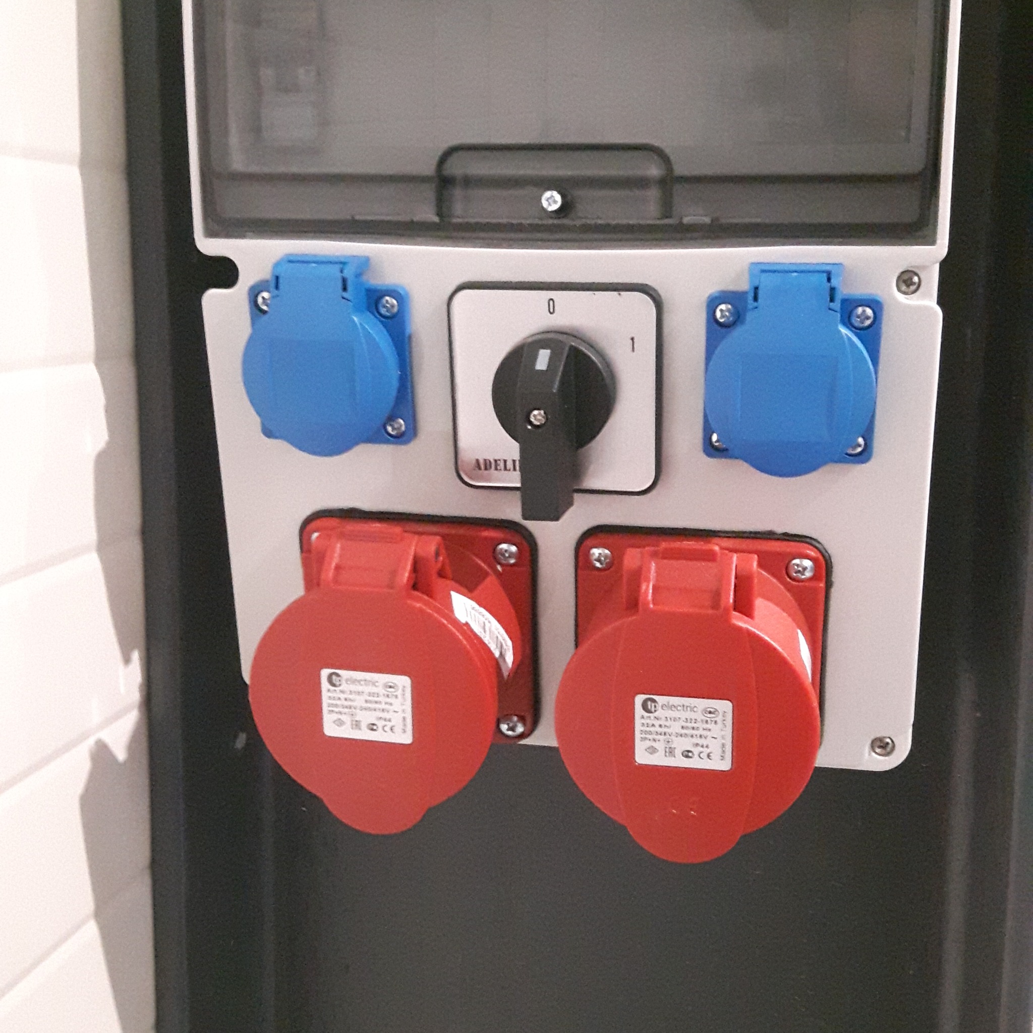 Gniazda siłowe przemysłowe, dwa czerwone i dwa niebieskie, zamontowane na białej płycie z przełącznikiem obrotowym w pozycji '0', widoczne etykiety z parametrami technicznymi.