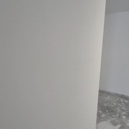 Damian Turcza Dampro - Świeżo pomalowana na biało ściana w Wieliczce, z widocznym grzejnikiem u dołu i fragmentem surowej podłogi w tle.