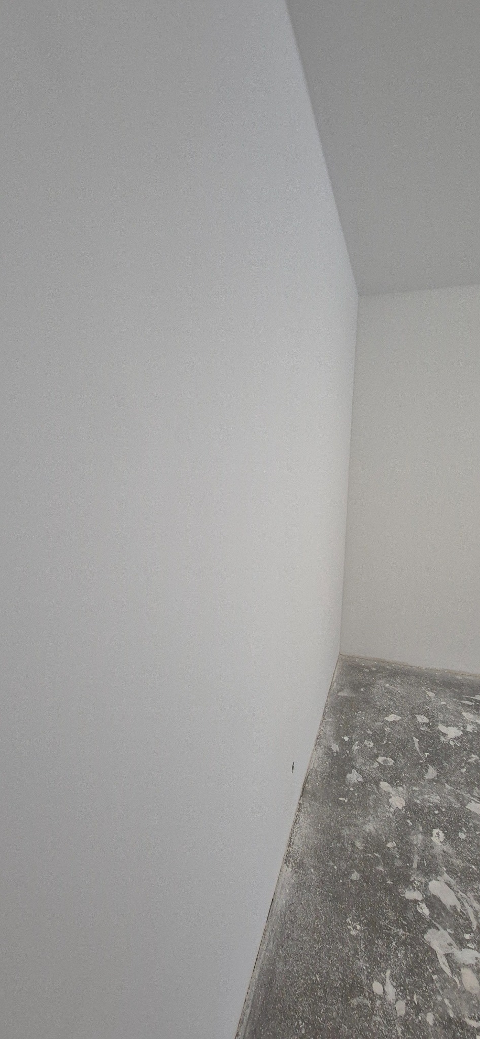 Wnętrze pokoju po nałożeniu gładzi, widoczny fragment ściany i podłogi z resztkami materiału budowlanego, narożnik ściany pod kątem.