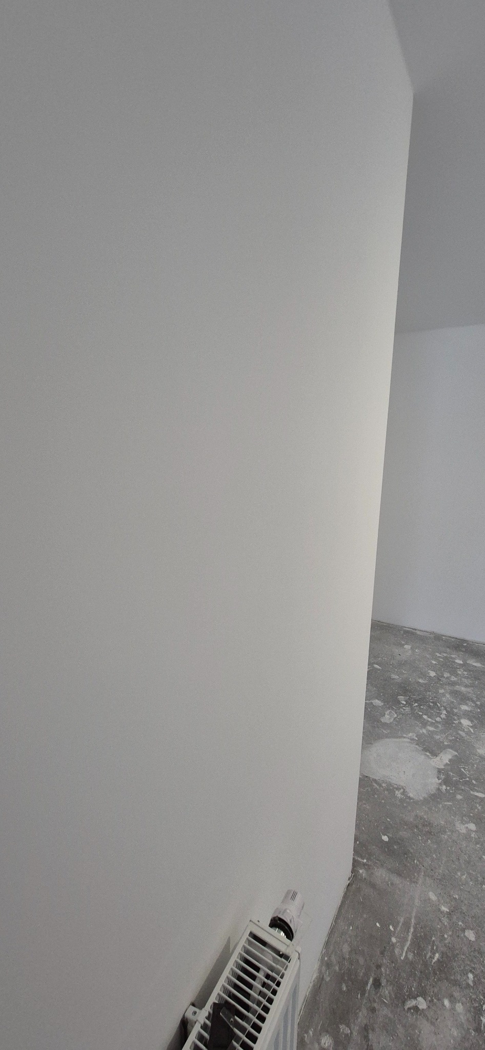 Świeżo pomalowana na biało ściana w Wieliczce, z widocznym grzejnikiem u dołu i fragmentem surowej podłogi w tle.