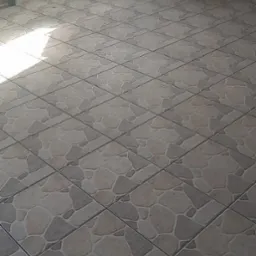 Beżowo-szara podłoga wyłożona płytkami ceramicznymi w kształcie nieregularnych kamieni, widok na fragment kuchni z szafką i kuchenką.