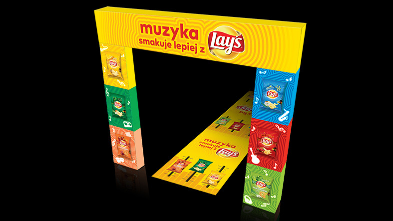 Promocyjna bramka z kartonów z logo Lays i hasłem 'Muzyka smakuje lepiej z Lays', z grafikami nawiązującymi do muzyki i smaków chipsów, ustawiona na podłożu imitującym klawiaturę pianina.