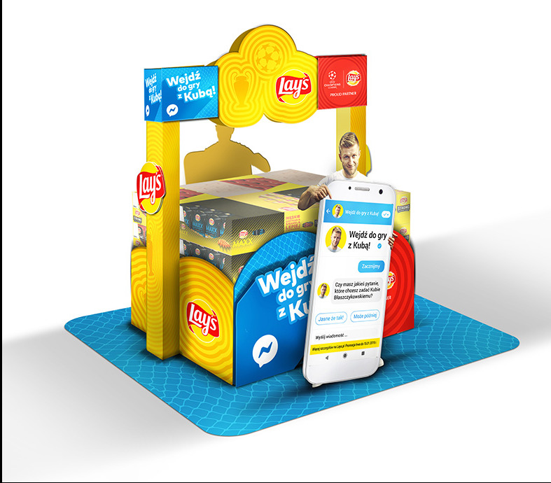 Ekspozytor reklamowy marki Lay's z motywem piłkarskim i wizerunkiem Jakuba Błaszczykowskiego, imitujący rozmowę na smartfonie, umieszczony na niebieskim podłożu z wzorem siatki.