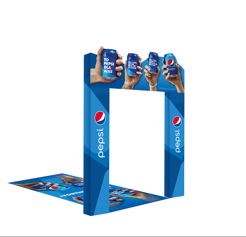 Niebieska brama reklamowa Pepsi z wizerunkami puszek trzymanych w dłoniach, umieszczona na podłodze z podobnym motywem, widok z przodu.