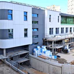 RUDBUD SP. z o.o. - Wielopiętrowy budynek w trakcie budowy, z widocznymi rusztowaniami, ociepleniem styropianowym i pracującym robotnikiem w oddali.