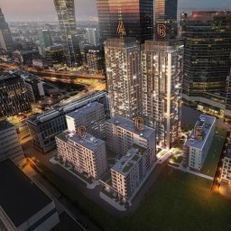 RUDBUD SP. z o.o. - Wizualizacja kompleksu budynków mieszkalnych z wysokimi wieżowcami w tle, widok z lotu ptaka o zmierzchu, z oświetlonymi oknami i zielenią wokół budynków.