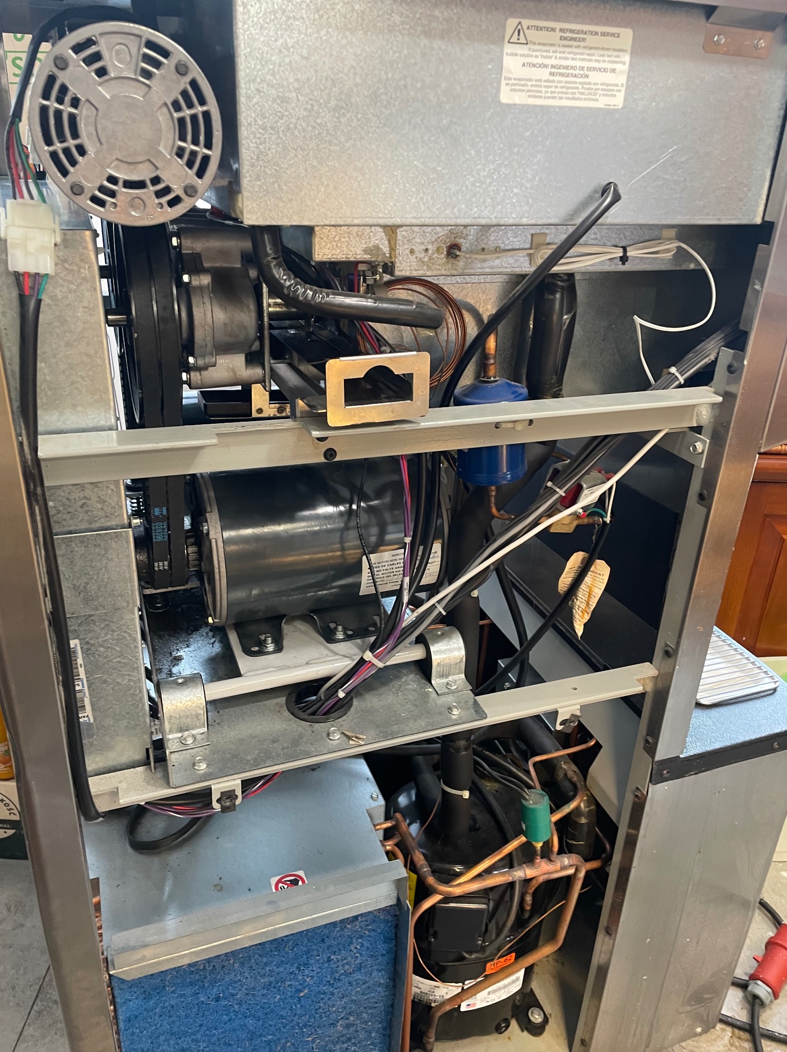 Wnętrze urządzenia chłodniczego z widocznym silnikiem, wentylatorem, przewodami i elementami instalacji chłodniczej, ukazane w trakcie przeglądu lub naprawy.