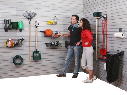 Zabudowa garażu z systemem paneli ściennych z haczykami i półkami, na których zawieszone są narzędzia ogrodnicze, sprzęt sportowy i akcesoria, prezentowana przez parę stojącą w rogu pomieszczenia.