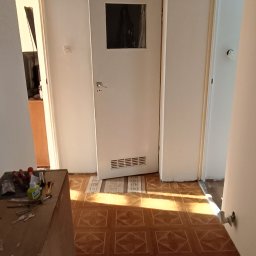 Klimek maluje - Korytarz w trakcie odnawiania z widocznymi narzędziami, białą ścianą, drzwiami z szybką i wzorzystą podłogą z płytek.