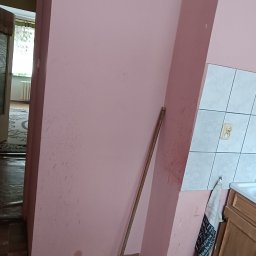 Klimek maluje - Różowa ściana w trakcie przygotowań do malowania, widoczne ślady zabrudzeń i szpachli, oparta o ścianę miotła, fragment płytek i szafki kuchennej w tle.