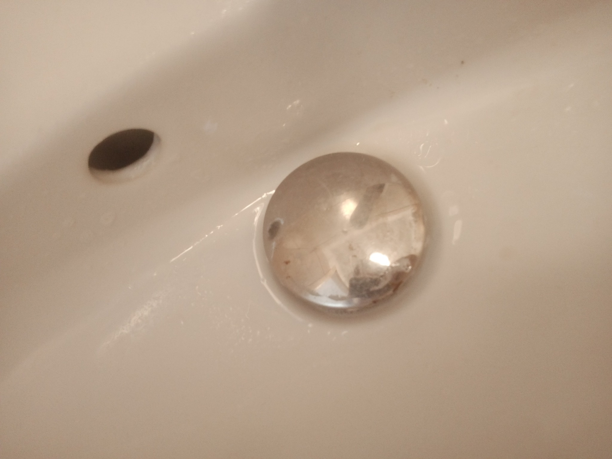 Umywalka z zatkanym odpływem i widocznym otworem przelewowym, na powierzchni widoczne zacieki i osad.