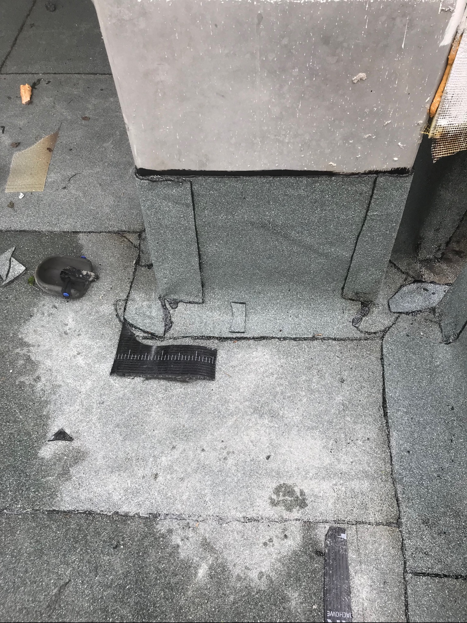 Fragment dachu z papy z widocznymi uszczelnieniami wokół komina, detale wykończeniowe i ślady po pracach dekarskich, w tym kawałki papy i resztki materiałów.