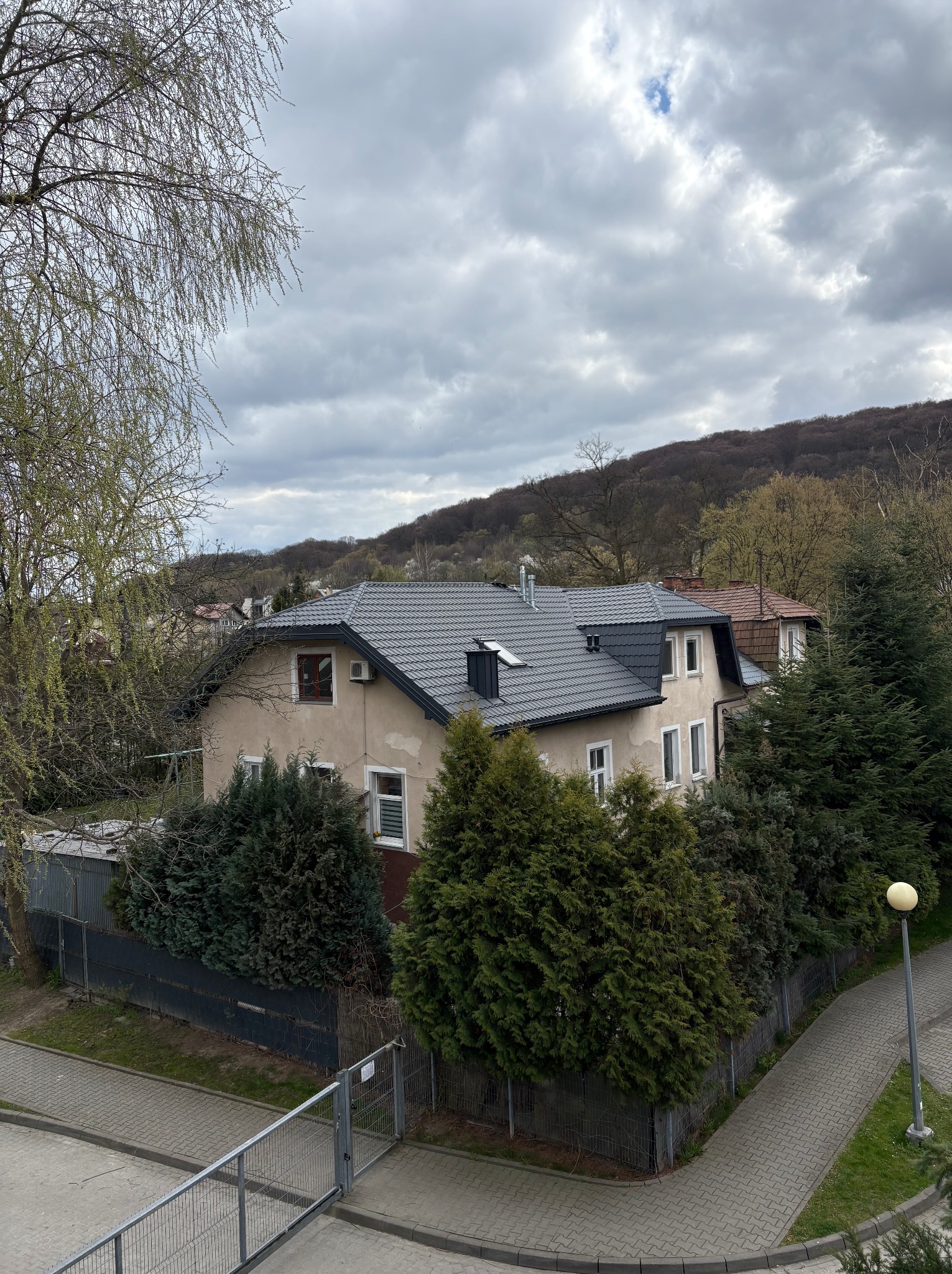 Dom z nowym, szarym dachem z dachówki ceramicznej, widoczny z góry, otoczony zielenią. Dach z oknami połaciowymi.