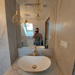 Grzegorz Siembida-Wykończenia wnętrz - Nowoczesna łazienka z owalną umywalką nablatową z baterią w kolorze złota, marmurowe płytki na ścianach i suficie oraz geometryczne lampy wiszące z metalu w kolorze złota, widoczne odbicie osoby...