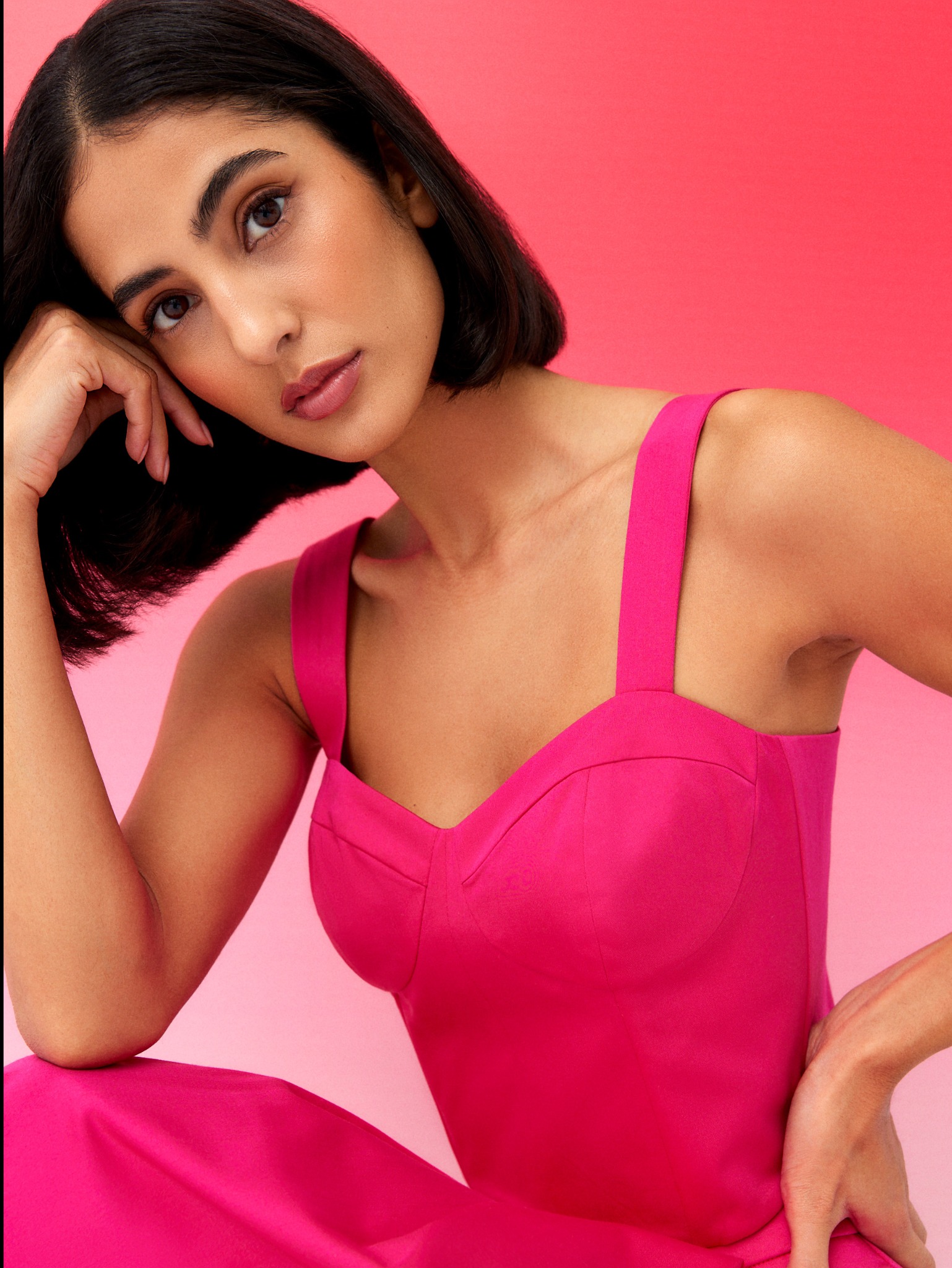 Portret kobiety z delikatnym, naturalnym makijażem, w różowej sukience na tle gradientu różu.