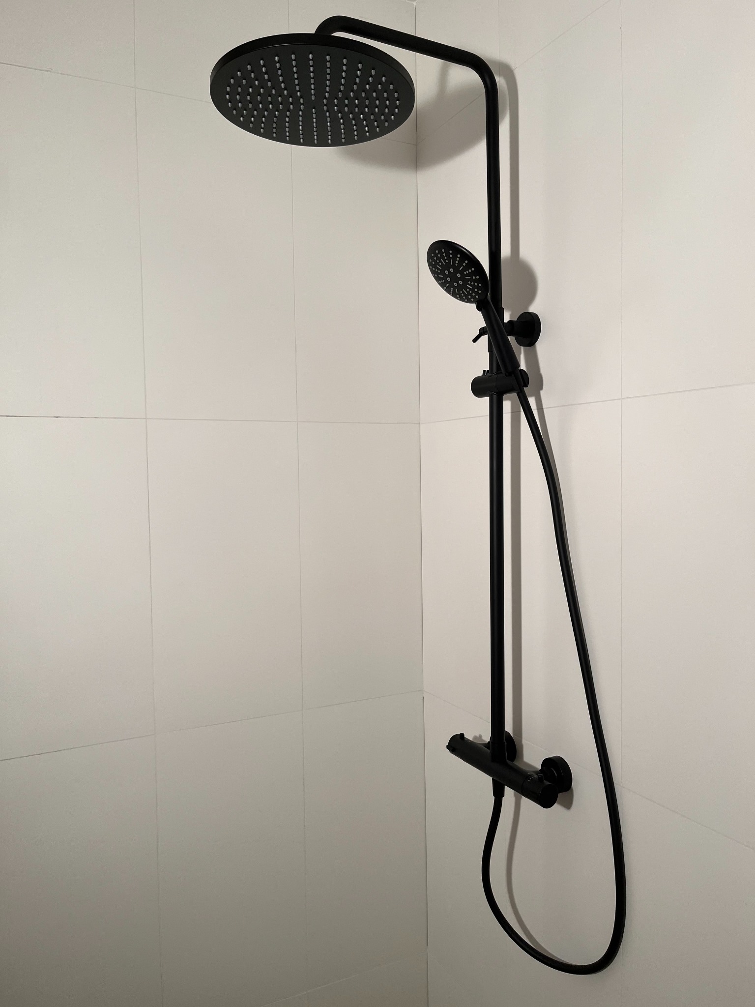 Czarna bateria prysznicowa z deszczownicą i słuchawką, zamontowana na ścianie z białych płytek. Minimalistyczny design, nowoczesna łazienka.