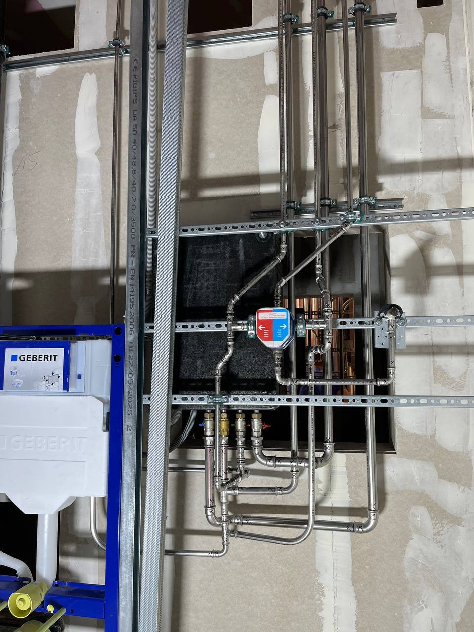 Instalacja wodno-kanalizacyjna w trakcie montażu: rury, zawory, stelaż podtynkowy Geberit. Widoczne elementy mocujące i surowa ściana w tle. Detal instalacji.