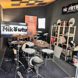 MIKOWHY DRUM SCHOOL MIKOŁAJ TOMZIK - Studio perkusyjne z zestawem perkusyjnym, wygłuszonymi ścianami, ekranem z logo szkoły perkusyjnej MikWhy Drum School i regałem z akcesoriami perkusyjnymi.