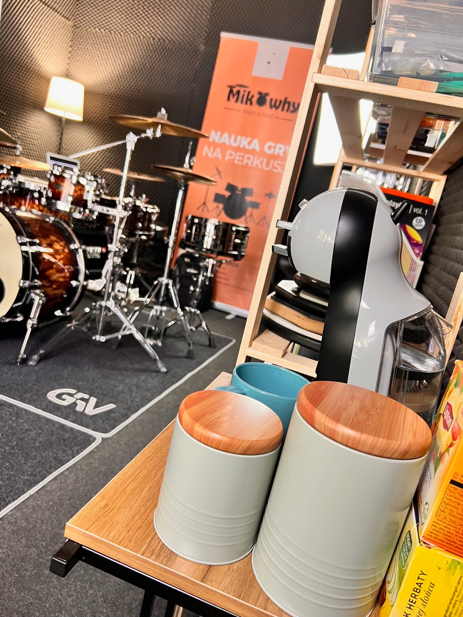 Sala do nauki gry na perkusji z zestawem perkusyjnym w tle, w kadrze widoczne akcesoria i plakat szkoły perkusyjnej MikWhy.