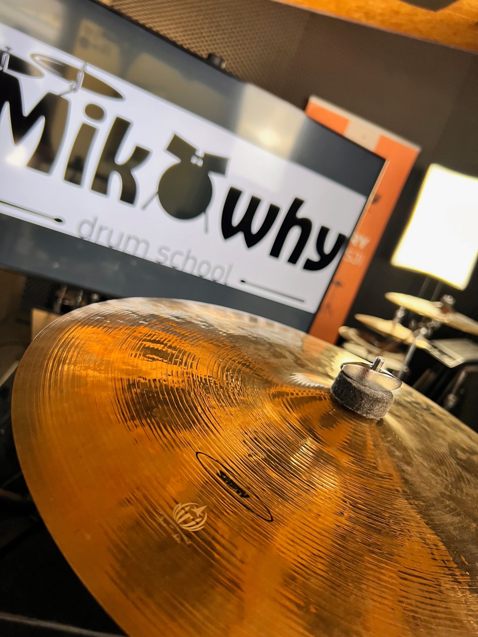 Błyszczący, złoty talerz perkusyjny z filcowym podkładem, w tle logo szkoły perkusyjnej MikWhy na monitorze.