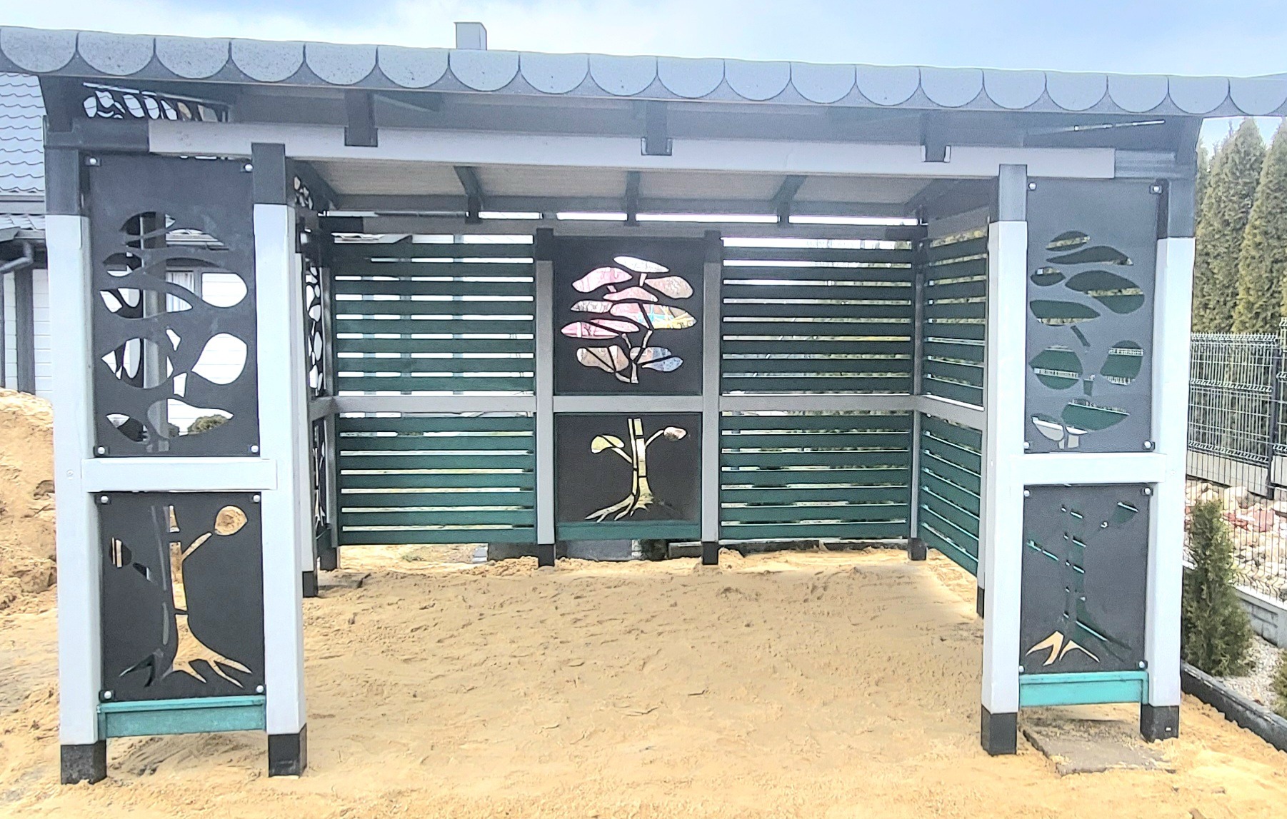 Nowoczesna altana z zielonymi panelami i dekoracyjnymi, wycinanymi motywami roślinnymi, wypełniona piaskiem.