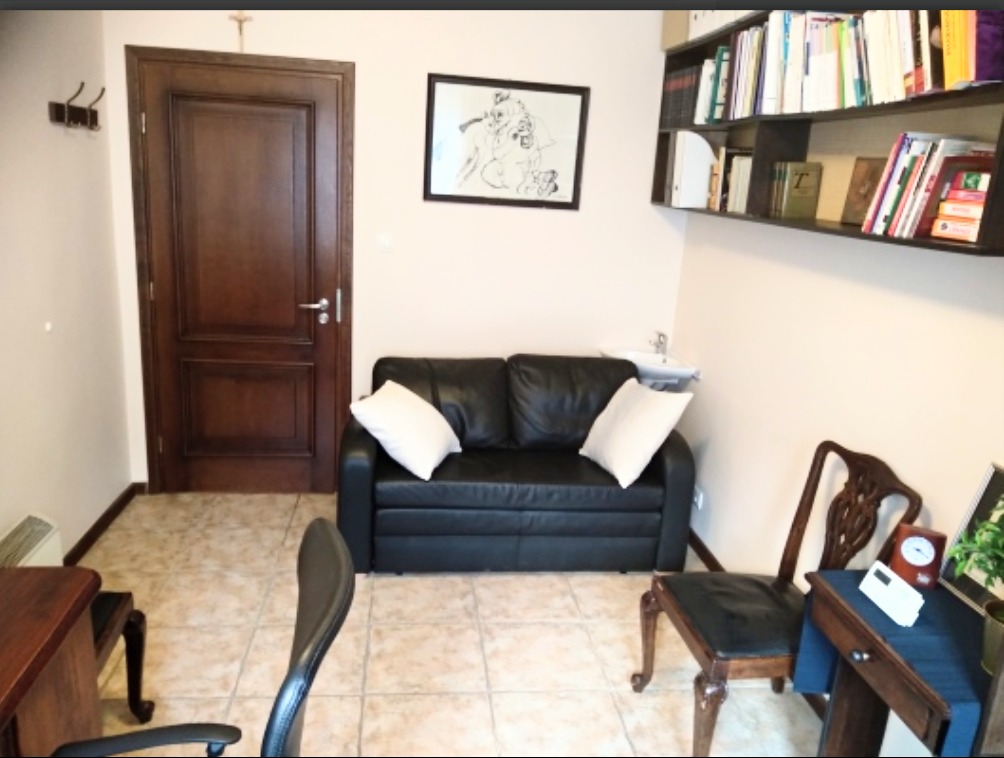 Gabinet w Gdańsku z czarną skórzaną sofą, białymi poduszkami, drewnianym biurkiem, krzesłem i półką z książkami, oświetlony ciepłym światłem.